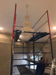 An electrician from Neptune Electric LLC installing a large chandelier from scaffolding in Las Vegas, NV