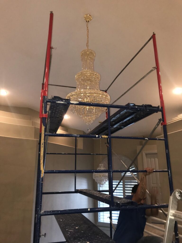An electrician from Neptune Electric LLC installing a large chandelier from scaffolding in Las Vegas, NV