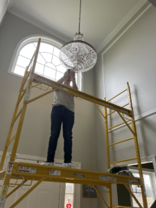 An electrician from PnP Electric on scaffolding installing a large chandelier in a high-ceiling home in Middletown, DE.