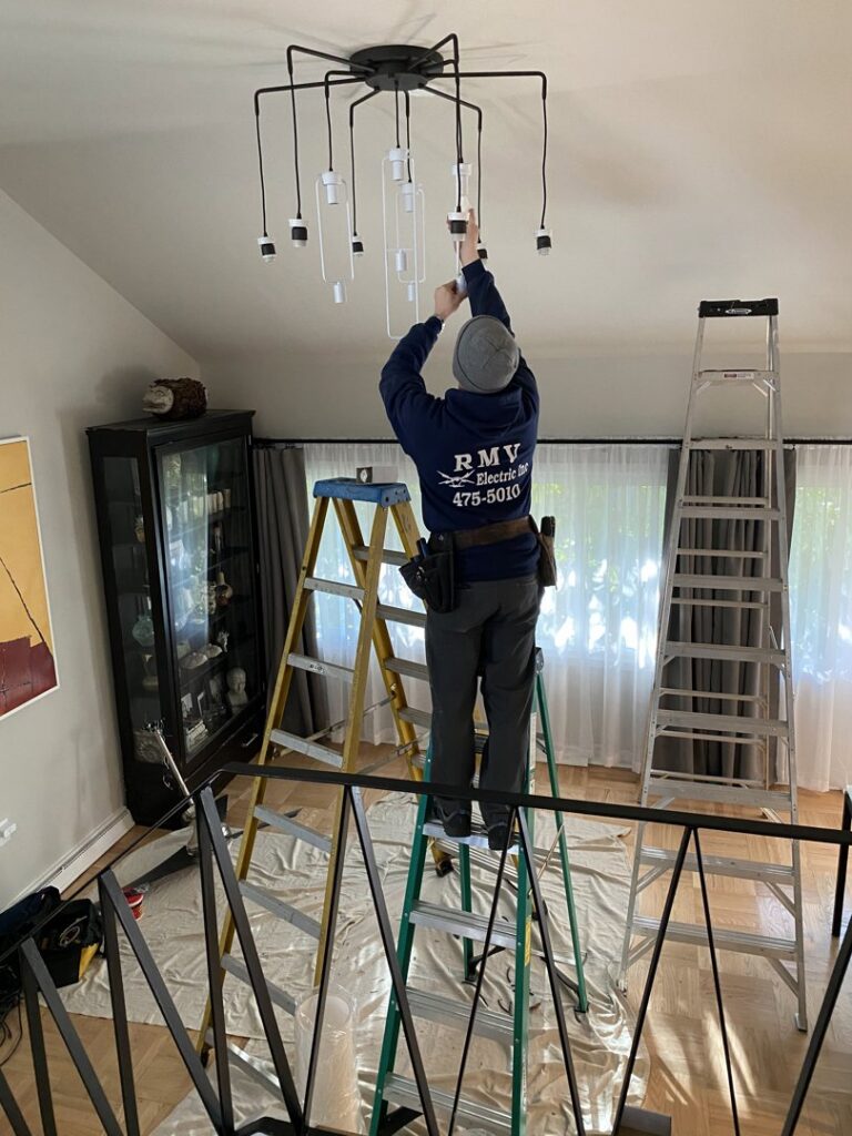 An electrician from RMV Electric installing a modern chandelier in a home in Wilmington, DE.
