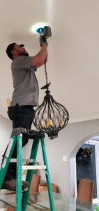 An electrician from Shark Electric installing a decorative chandelier in a home in Houston, TX.
