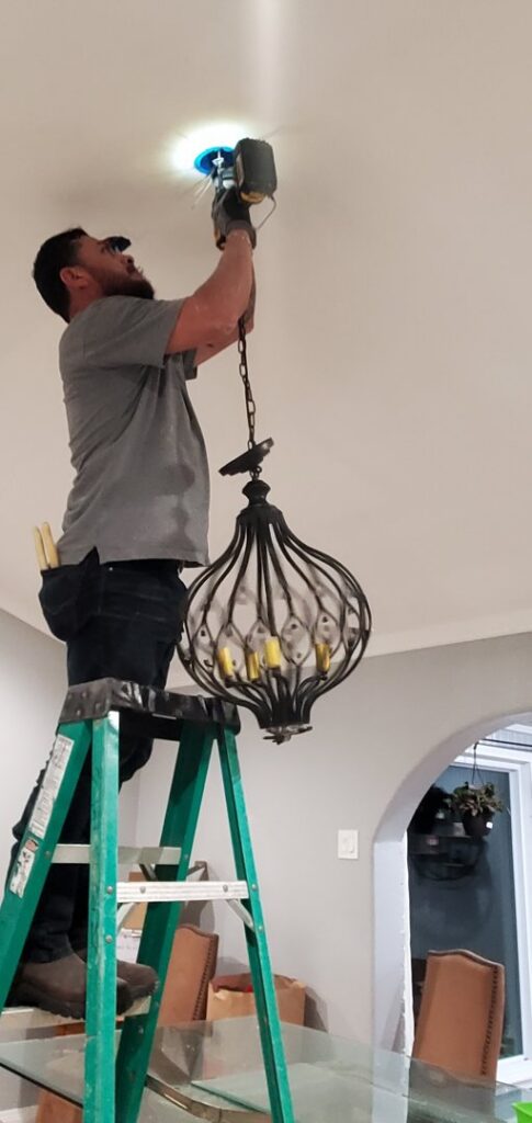 An electrician from Shark Electric installing a decorative chandelier in a home in Houston, TX.