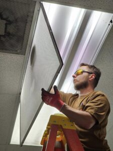 An electrician from Bee Thumb Electric in North Highlands, CA, installing a commercial fluorescent light fixture.