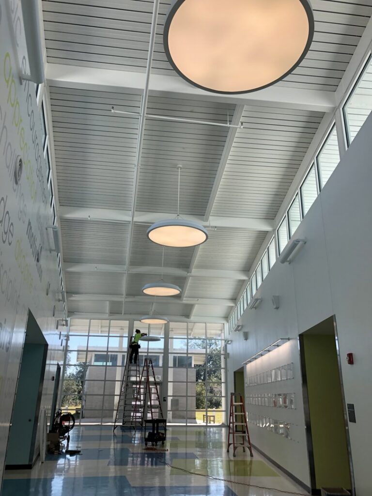 An electrician on a ladder installing overhead lighting in a commercial hallway for T.E.C Electrical Contracting, LLC in Jacksonville, FL