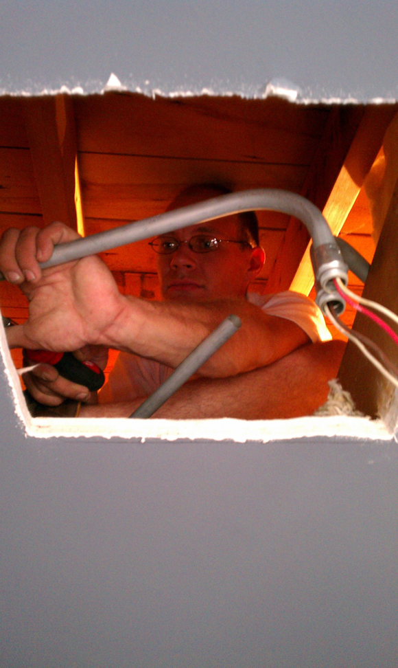 An electrician installing electrical conduit and wiring through a ceiling opening for Hunsicker Electrical Services in Chicago, IL.