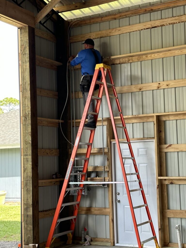 An electrician from Bee Electrical Contracting on a ladder installing conduit and wiring in a building in Port Saint Lucie, FL.