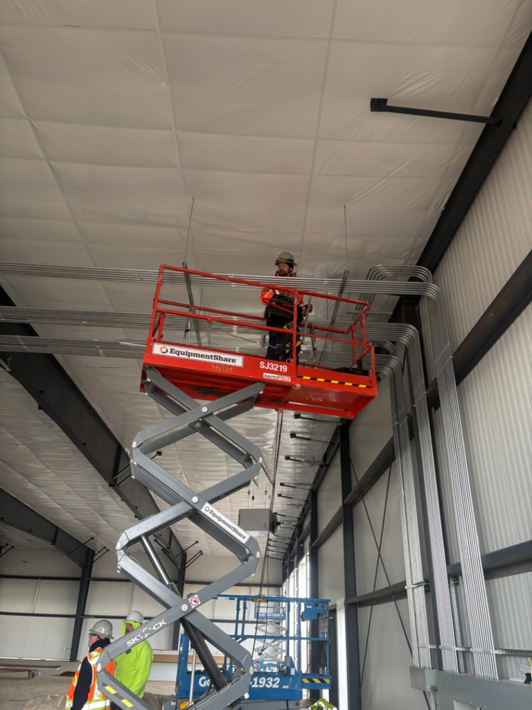 An electrician from Doherty Electric installing electrical conduits on a high ceiling in Meridian, ID.