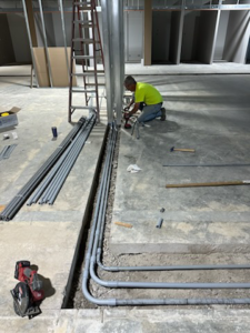An electrician installing electrical conduits in a floor trench for Nelson Electric in Brooklyn Park, MN