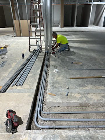 An electrician installing electrical conduits in a floor trench for Nelson Electric in Brooklyn Park, MN