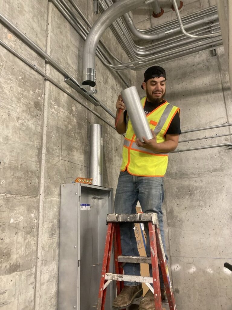 An electrician installing electrical conduits and a panel on a concrete wall for Electrical Power Source in Fresno, CA.