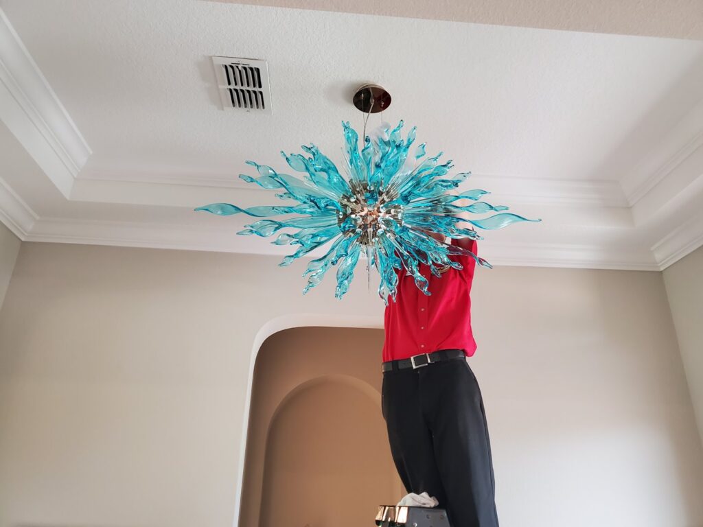 An electrician on a ladder installing a decorative blue light fixture for Small Jobs Electric in Tampa, FL.