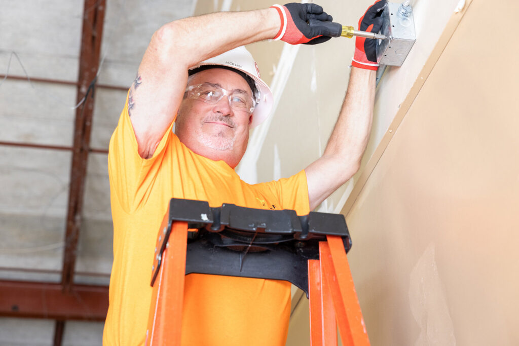 An electrician from Tenax Electrical Company installing an electrical box on a wall in Jacksonville, FL.