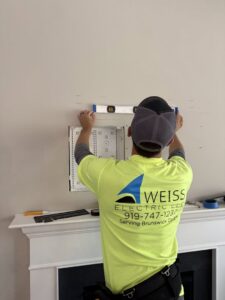 An electrician from Weiss Electric LLC installing an electrical box above a fireplace mantel in Saint Charles, MO.