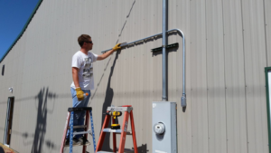 An electrician on a ladder installing electrical conduit on the exterior of a building for Northern Lights Electric Company in Sheridan, WY.