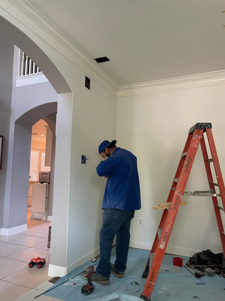 An electrician from Powered By H installing an electrical outlet or switch box in a home in Houston, TX.