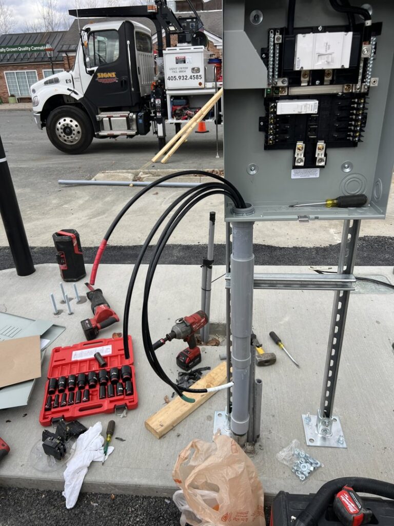 An electrician installing an outdoor electrical panel and wiring, with tools on the ground, for Peeler Electric Light & Power in Merrimack, NH.