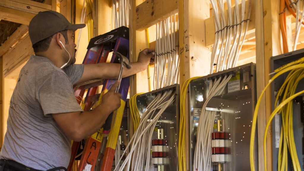 An electrician installing electrical panels and wiring in a framed wall for Colonial Electric LLC in Scottsdale, AZ.