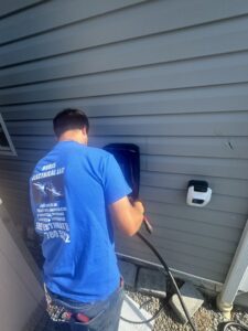 An electrician from Rudis Electrical LLC installing an electric vehicle charging station on a home exterior in Scranton, PA.