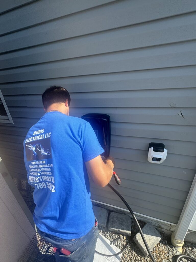 An electrician from Rudis Electrical LLC installing an electric vehicle charging station on a home exterior in Scranton, PA.