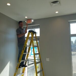 An electrician from Fuller Electrical Contractors, Inc. installing an exit sign and lighting in a commercial building in Oldsmar, FL.