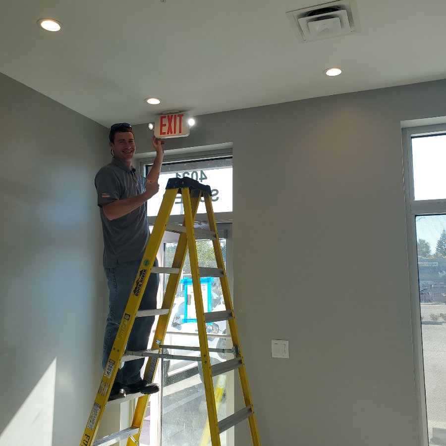 An electrician from Fuller Electrical Contractors, Inc. installing an exit sign and lighting in a commercial building in Oldsmar, FL.
