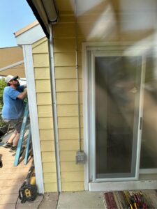 An electrician on a ladder installing exterior conduit and wiring on a house, performed by Legacy Electric in Westminster, CO.