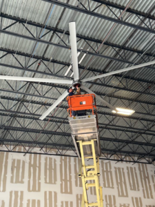 An electrician installing a large industrial ceiling fan from a scissor lift for Electric Service & Repair, Inc in Miami, FL.