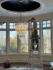 An electrician from Amped Electric installing a large, multi-tiered chandelier in Virginia Beach, VA.
