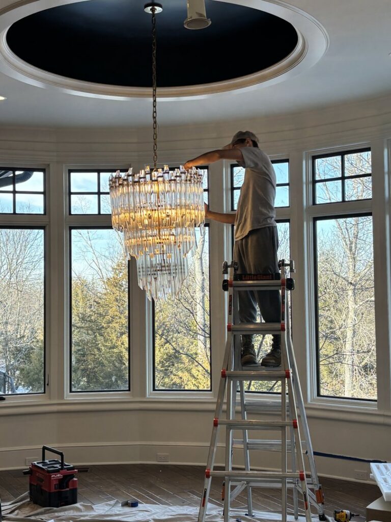 An electrician from Amped Electric installing a large, multi-tiered chandelier in Virginia Beach, VA.