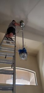 An electrician on a ladder installing a large chandelier for Star Light Electric LLC in Phoenix, AZ