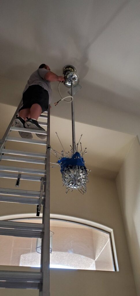 An electrician on a ladder installing a large chandelier for Star Light Electric LLC in Phoenix, AZ