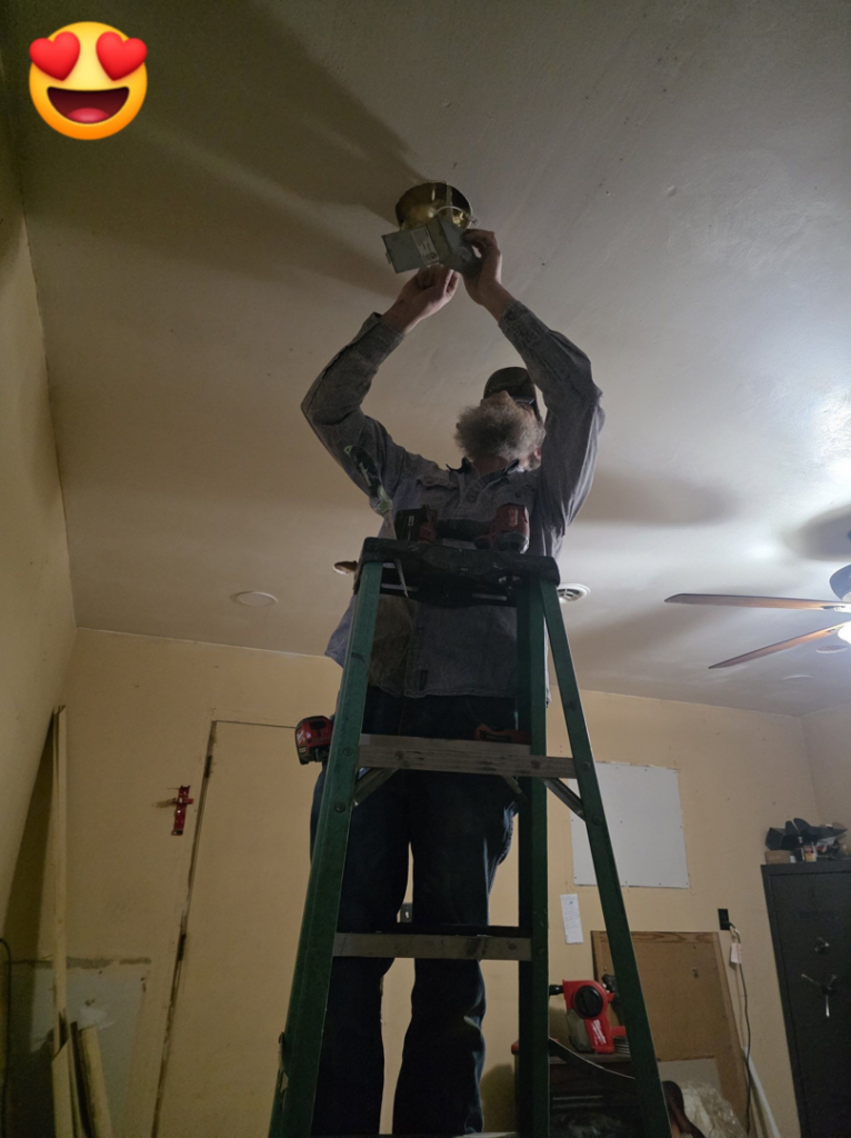 An electrician from 3E Enterprises, LLC installing a new light fixture on a ceiling in Washburn, MO.