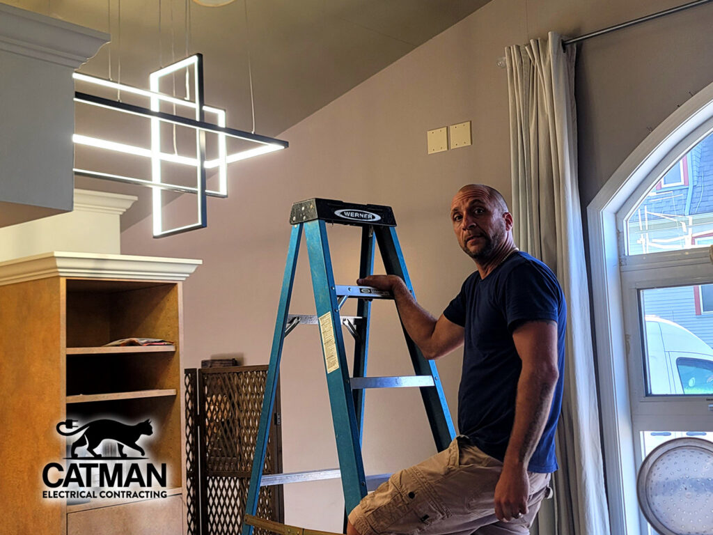 An electrician on a ladder installing a modern light fixture, performed by Catman Electrical Contracting in Dallas, PA.