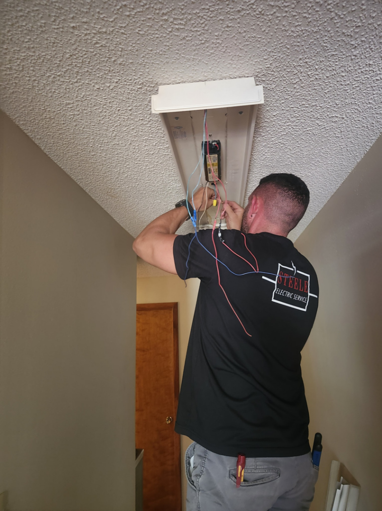 An electrician installing a light fixture for a client at Steele Electric Service in Forest Grove, OR.