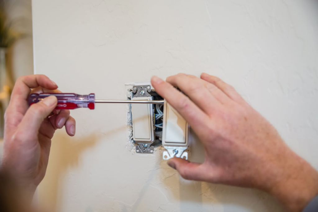 An electrician installing or repairing a light switch with a screwdriver for Jarvie Electric in Rochester, NY.