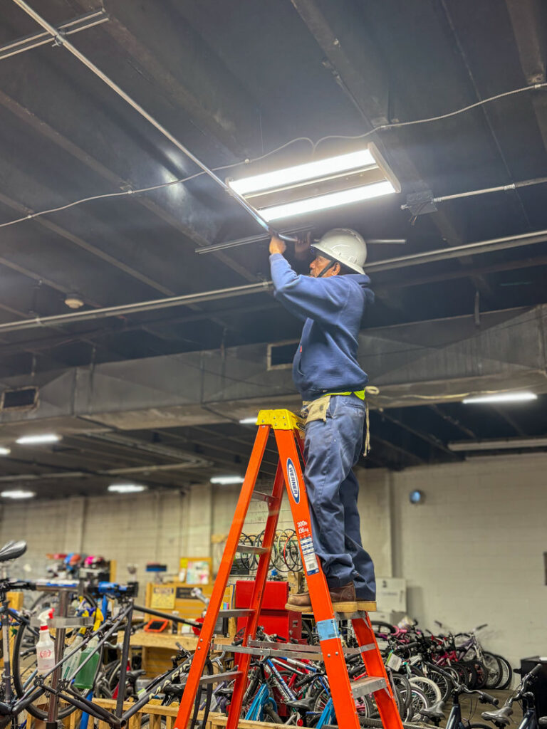 An electrician on a ladder installing or repairing an overhead light fixture, a service provided by Carolina Voltage in Charlotte, NC.