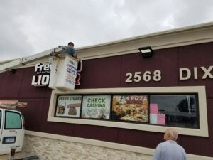 An electrician from MDEC Electrical & Lighting installing a new sign for a liquor store in Livonia, MI.