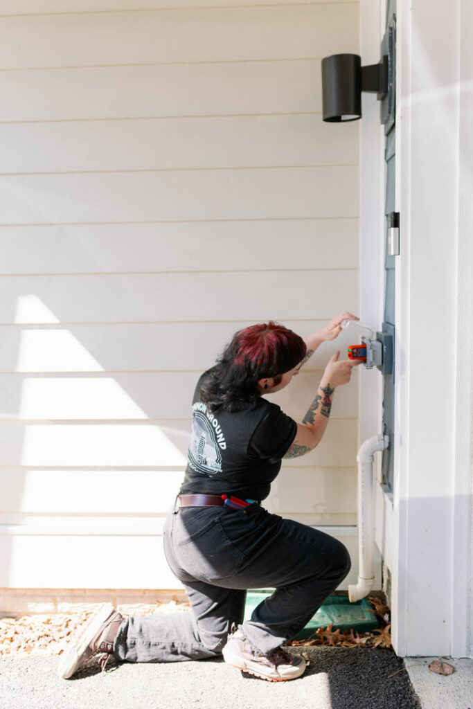 An electrician installing an outdoor electrical box or fixture on a home exterior for Common Ground Electrical in Baltimore, MD.