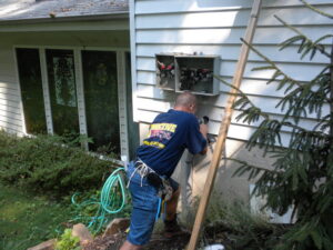 An electrician from Conductive Electrical Contracting installing an outdoor electrical panel on a house in Smyrna, DE.