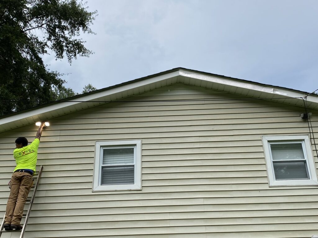 An electrician from High Electrical installing an outdoor floodlight on a ladder in Atlanta, GA.
