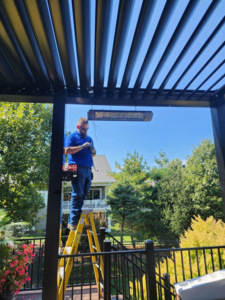 An electrician from ATW Electric on a ladder installing an outdoor patio heater in Kansas City, MO.