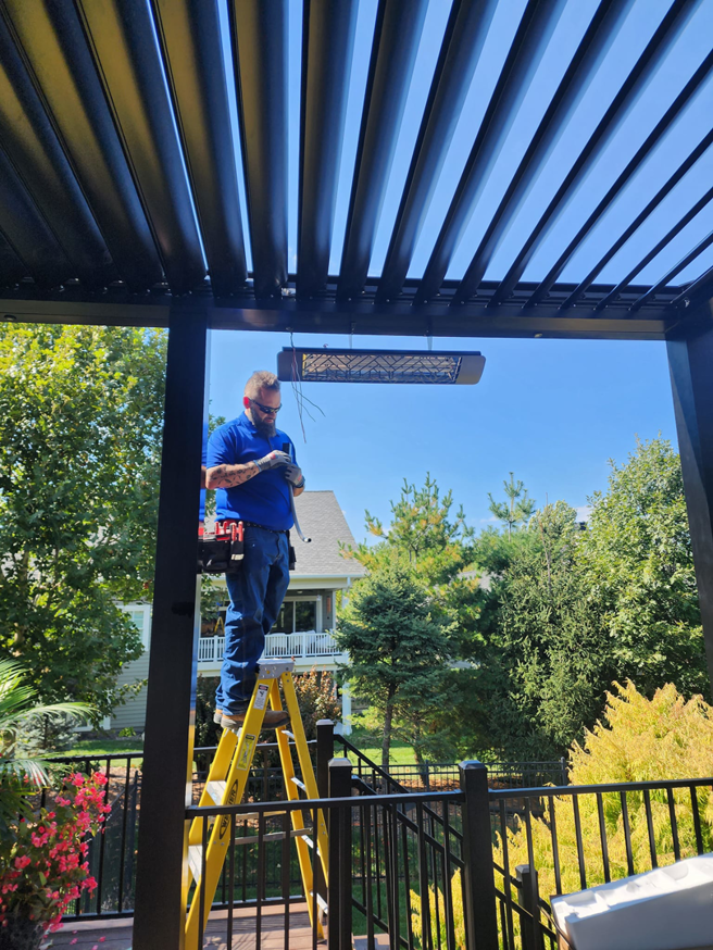 An electrician from ATW Electric on a ladder installing an outdoor patio heater in Kansas City, MO.