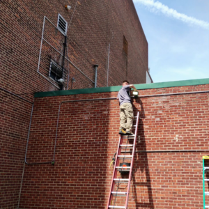 An electrician installing an outdoor light fixture on a brick building for C&J And Sons Multi Services in Newark, NJ.
