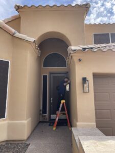 An electrician on a ladder installing an outdoor light fixture near a garage door for Miller and Sons Electric in North Myrtle Beach, SC.