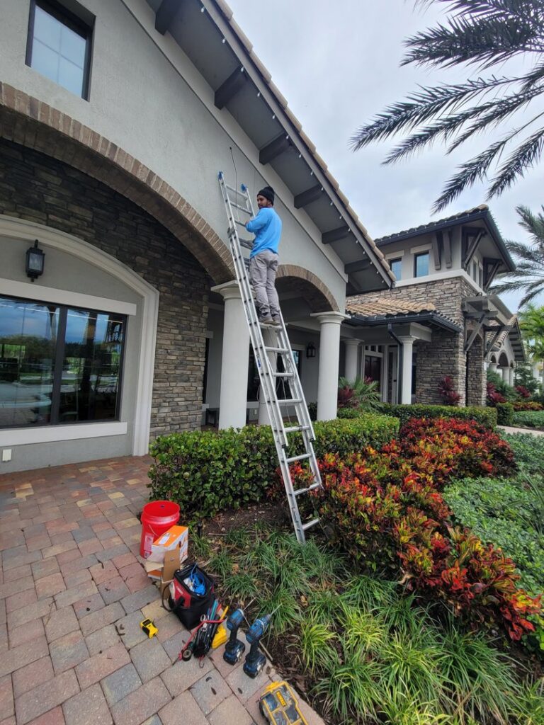 An electrician on a ladder installing outdoor lighting at a property by Wirenut Technologies LLC in Brandon, FL