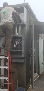 An electrician on a ladder installing wiring in an outdoor electrical box for F & L Electrical, LLC in Clemmons, NC.