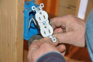 Close-up of an electrician's hands installing a new electrical outlet into a blue box for Beaver Electric in Hillsboro, OR.