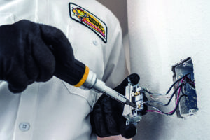 An electrician from Mister Sparky Kansas City, MO, installing an electrical outlet with a screwdriver.