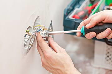 An electrician installing an electrical outlet with a screwdriver for Reliable Electric in Olympia, WA.