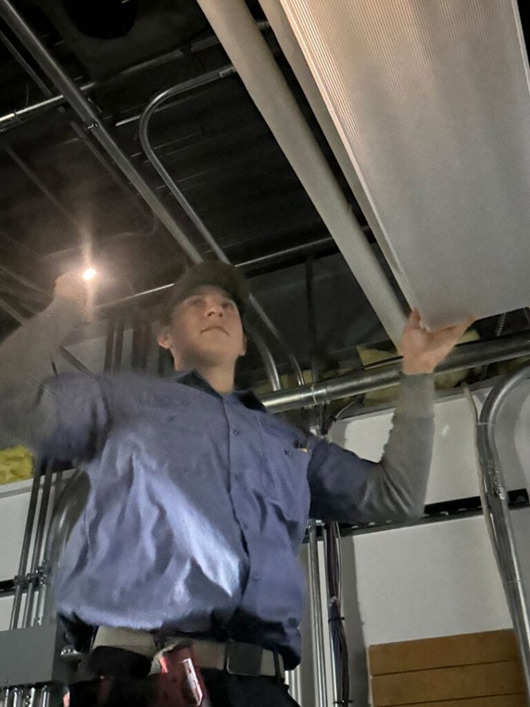 An electrician installing or adjusting an overhead light fixture at Three Rivers Electric in Fort Wayne, IN.
